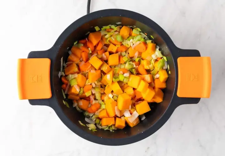 Trozo de calabaza, zanahoria y puerro picados en una olla, listos para hacer una deliciosa crema de verduras.