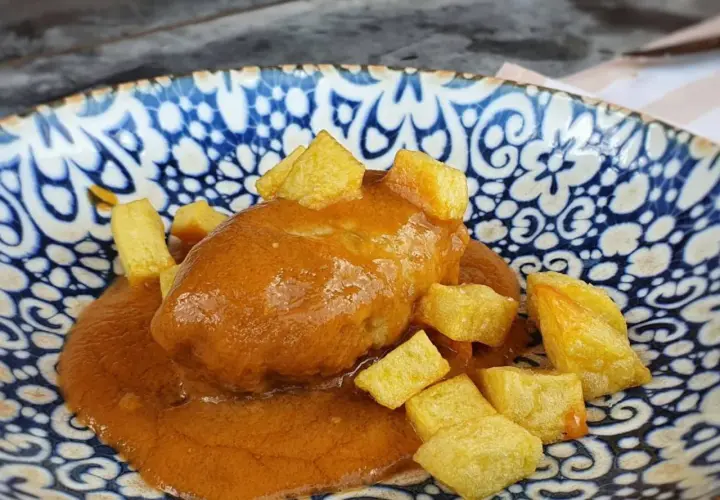 Rollo de bonito en salsa con patatas fritas, servido en un plato azul y blanco.