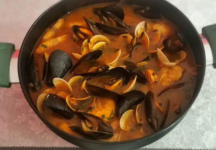 Caldereta de pescado humeante en una olla, repleta de mejillones, almejas y trozos de pescado en una rica salsa roja.