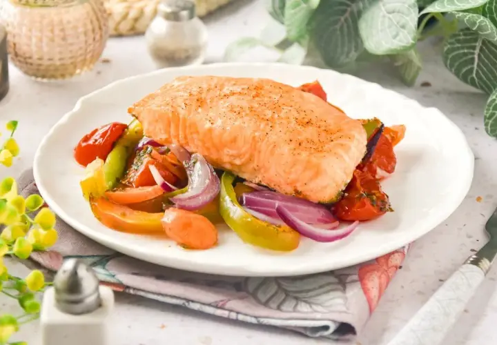 Delicioso salmón al horno con verduras coloridas: tomates, pimientos y cebolla morada. Un plato saludable y lleno de sabor.