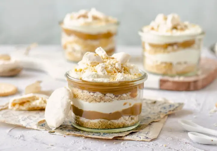 Postres en vaso con capas de galleta, crema y dulce de leche. Coronados con merengue y un toque de polvito canario.