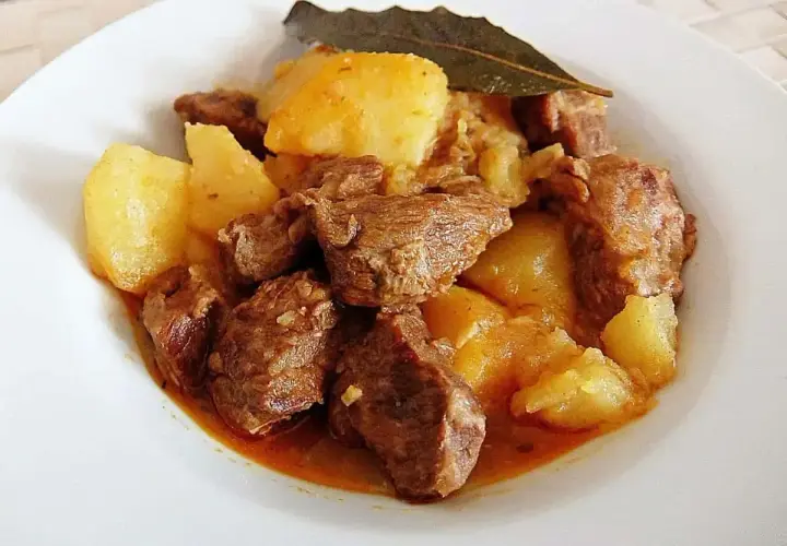 Plato de morcillo de ternera estofado con patatas y una hoja de laurel.