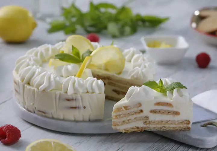 Deliciosa tarta de limón sin horno, con capas de galleta y crema, decorada con merengue, rodajas de limón y menta.