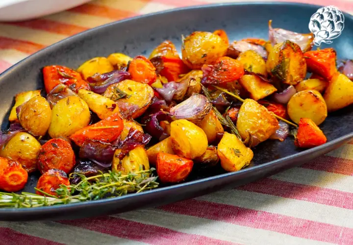 Un plato de verduras al horno, con patatas, zanahorias y cebolla morada, adornado con romero fresco.