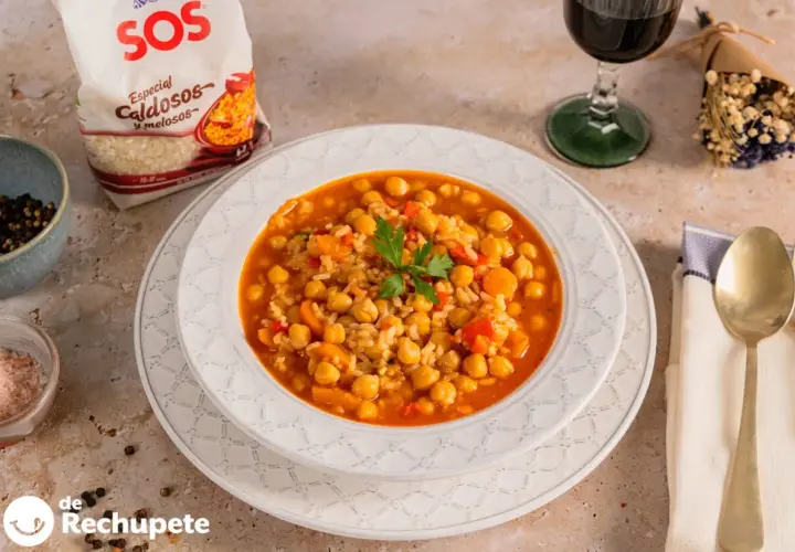 Plato de garbanzos con arroz, pimientos y zanahoria, decorado con perejil. Acompañado de una copa de vino tinto y una bolsa de arroz SOS.