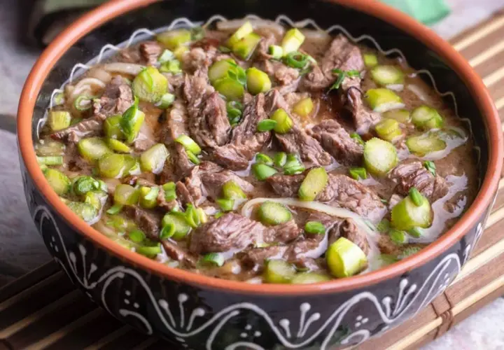 Un reconfortante plato de ternera guisada con trozos de carne tierna, fideos y espárragos verdes, servido en un cuenco rústico.
