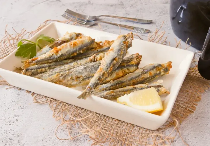 Boquerones crujientes en freidora de aire, servidos en plato blanco con limón y perejil.