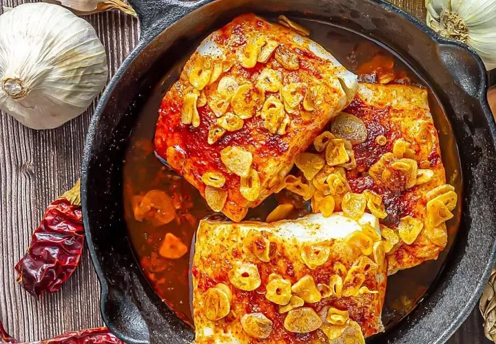 Bacalao ajoarriero en cazuela de hierro fundido, con ajos laminados dorados y guindillas secas.