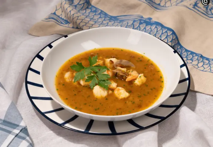 Un plato de sopa de pescado con trozos de marisco, gambas y mejillones, decorado con perejil fresco.