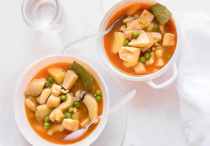 Dos cuencos de sepia con patatas y guisantes en salsa. Un vaso de agua al lado.