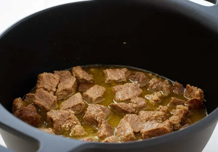 Trozos de magro con tomate cocinándose en una olla negra.
