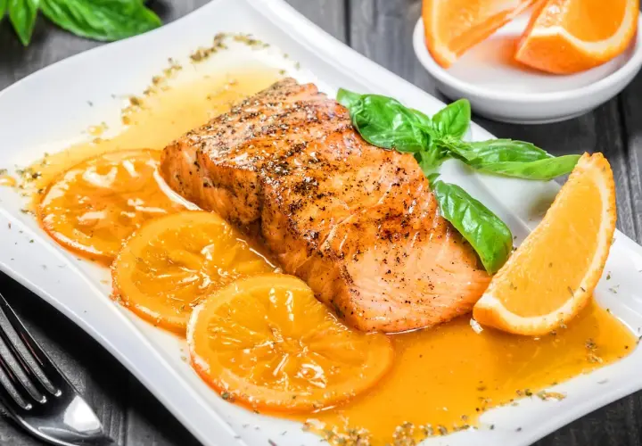 Delicioso salmón a la naranja, servido con rodajas de naranja y hojas de albahaca fresca.