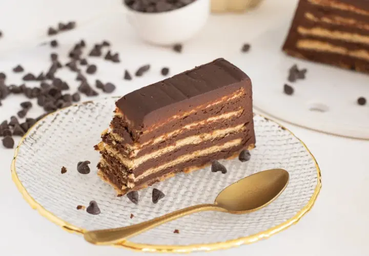 Rebanada de tarta de galletas de la abuela, con capas de galleta y chocolate, decorada con chispas de chocolate y una cuchara dorada.