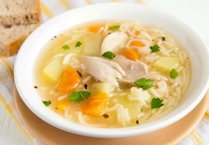 Un reconfortante plato de sopa de pollo con fideos, trozos de zanahoria y patata, adornado con perejil fresco.