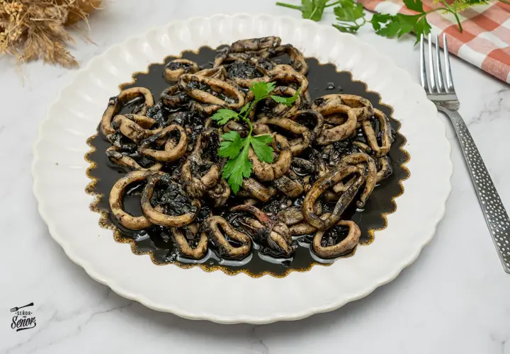 Calamares en su tinta, una receta tradicional servida en un plato blanco con un tenedor y perejil fresco.