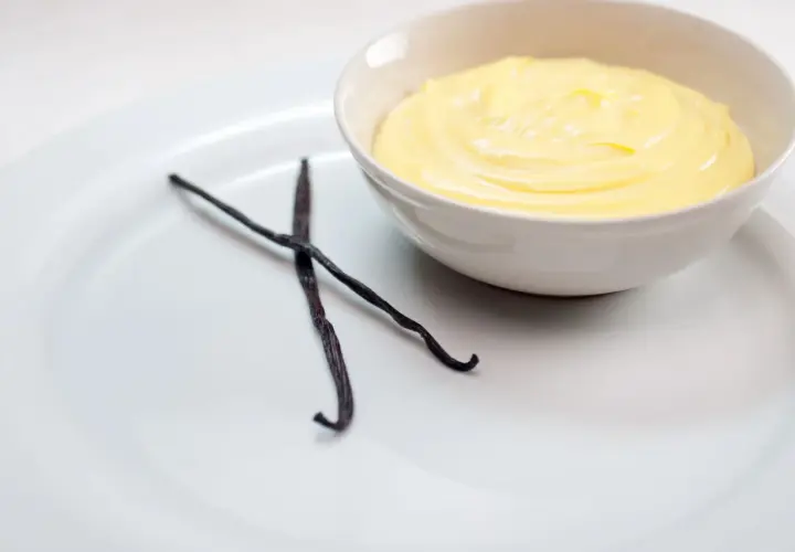 Crema inglesa cremosa en un tazón, con dos vainas de vainilla oscuras al lado.