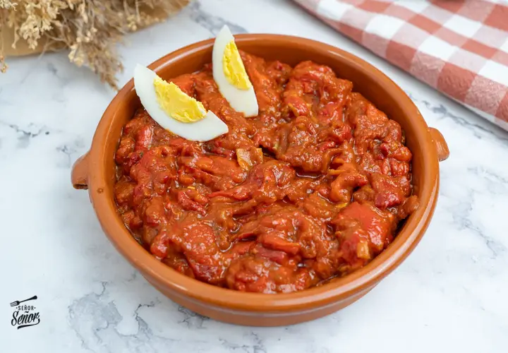 Un sabroso asadillo manchego en cazuela de barro, decorado con gajos de huevo cocido.