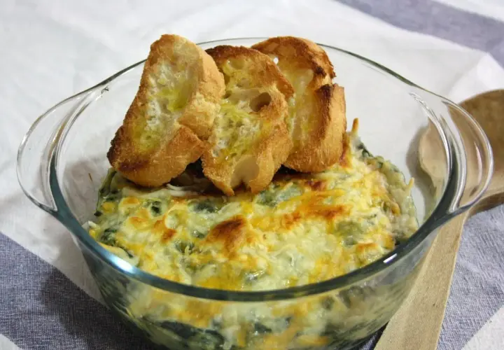 Delicioso plato de espinacas con bechamel gratinado, coronado con tostadas de pan.