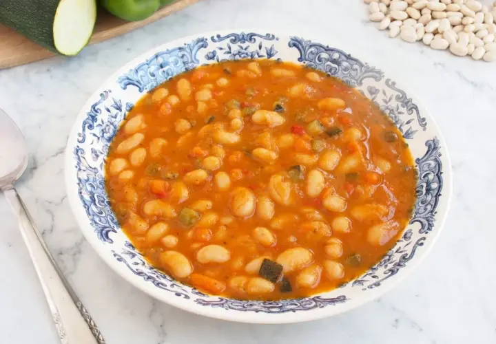 Un plato de alubias blancas con verduras, cocinadas en una salsa sabrosa. Se ven trozos de pimiento, zanahoria y calabacín.
