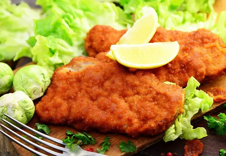 Dos filetes empanados dorados, servidos con lechuga fresca, limones y coles de Bruselas. Un plato delicioso y crujiente.