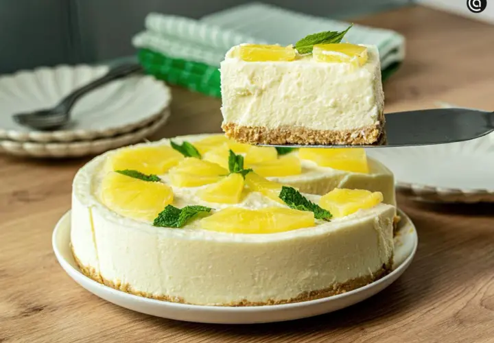 Una porción de tarta de piña sin horno, cremosa y decorada con piña y menta, se levanta de la tarta completa.