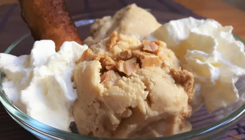 Delicioso helado de turrón con trozos crujientes, acompañado de nata montada y un bizcocho dorado.
