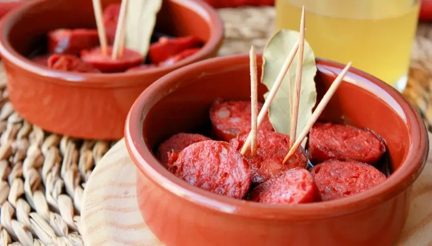Dos cuencos de barro con chorizos a la sidra, decorados con palillos y hojas de laurel.