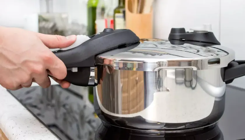 Mano cerrando la tapa de una olla express para cocinar lentejas. Cocina rápida y sabrosa.