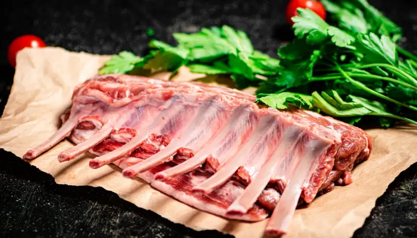 Costillar de cordero crudo, listo para preparar un delicioso cordero al chilindrón con perejil y tomates.