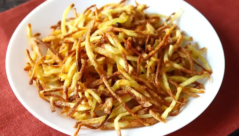 Un plato blanco lleno de crujientes patatas paja doradas, listas para ser disfrutadas.