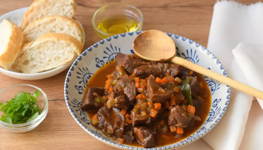Un reconfortante plato de ternera en salsa, con trozos tiernos de carne, zanahoria y apio, servido con pan y perejil fresco.