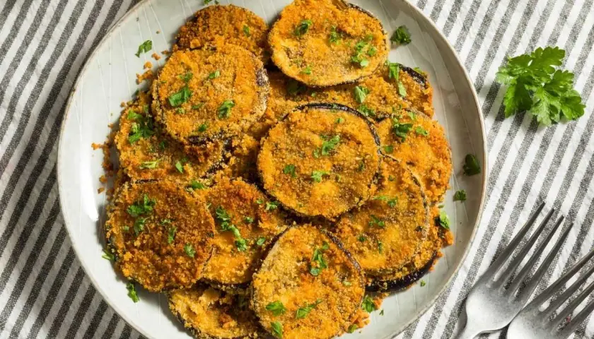 Plato de berenjenas rebozadas, doradas y crujientes, espolvoreadas con perejil fresco.