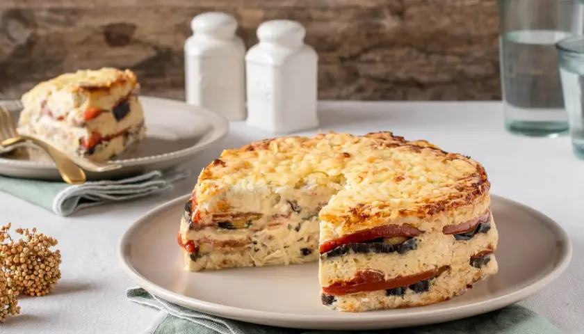 Pastel de verduras en capas, gratinado con queso, servido en un plato.