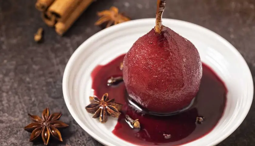 Peras al vino, cocinadas a la perfección, servidas en un plato blanco con especias como anís estrellado y canela.