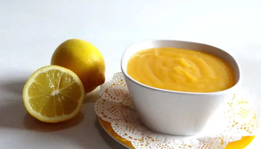 Un tazón de crema de limón, con limones frescos al lado.