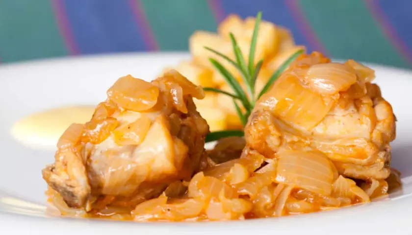 Dos trozos de conejo en escabeche, cubiertos de cebolla caramelizada, acompañados de patatas fritas y una ramita de romero.