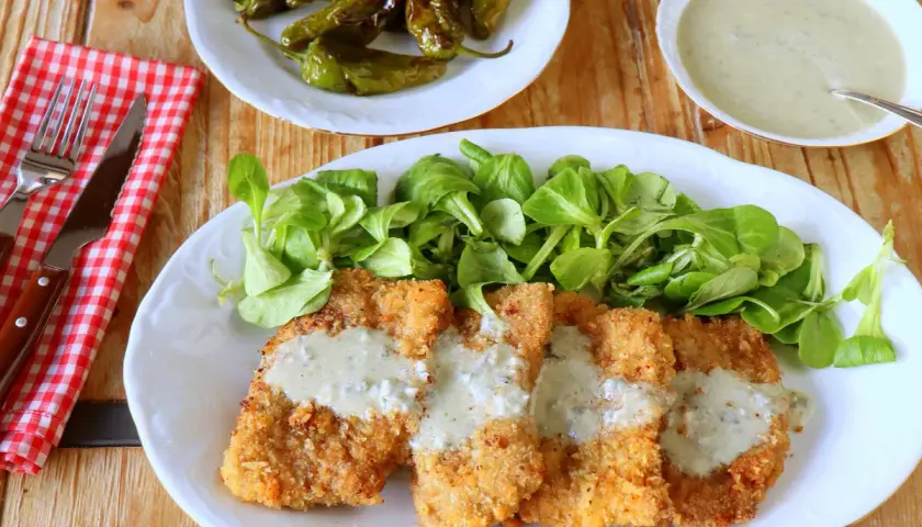 Escalopines al cabrales crujientes, servidos con ensalada verde y pimientos asados. ¡Un plato delicioso!