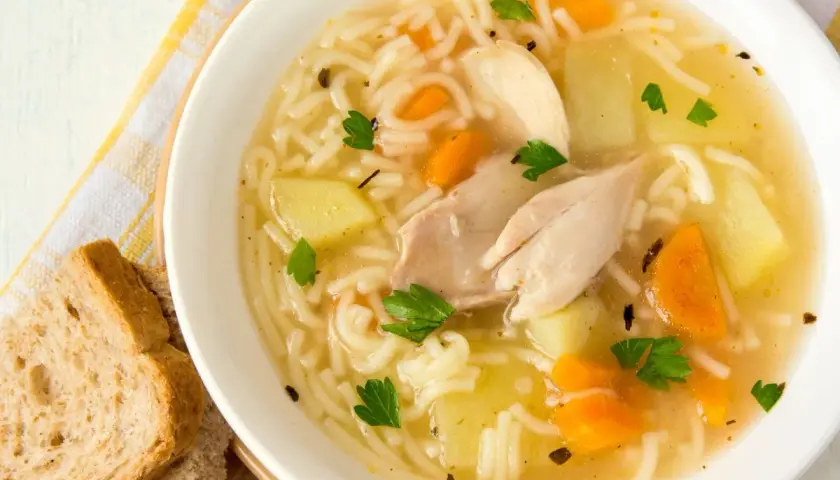 Un reconfortante plato de sopa de pollo receta, con fideos finos, trozos de pollo, patatas y zanahorias, adornado con perejil fresco.