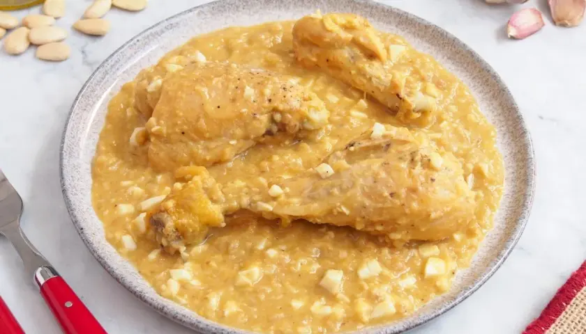 Pollo a la pepitoria servido en un plato, con trozos de huevo duro y almendras esparcidas.
