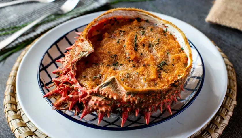 Txangurro a la donostiarra, un delicioso relleno de marisco gratinado en su propio caparazón, adornado con perejil picado.