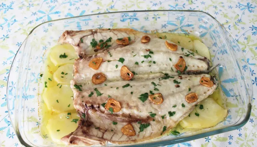 Lubina a la espalda horneada con patatas, ajo y perejil en una fuente de cristal.