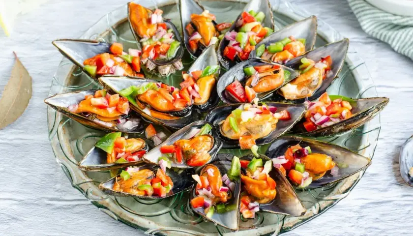 Mejillones a la vinagreta, frescos y coloridos, servidos en una bandeja de cristal.