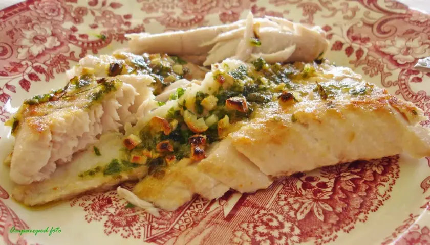 Deliciosa ventresca al horno, jugosa y dorada, con un aderezo verde de hierbas y ajo.