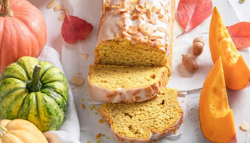 Bizcocho de calabaza, receta de la abuela, con glaseado y almendras. Rodeado de calabazas y hojas de otoño.