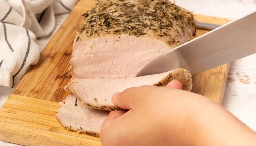 Un jugoso lomo a la sal, recién horneado y cubierto de hierbas, se corta en rodajas tiernas sobre una tabla de madera.