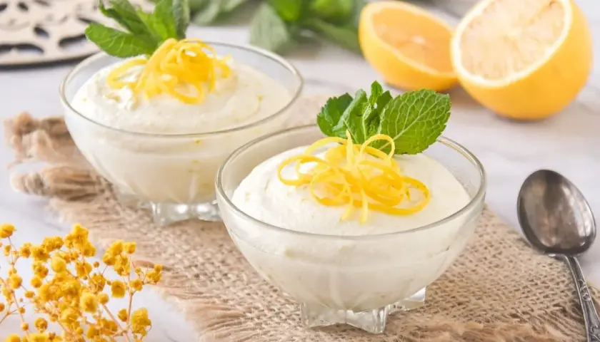 Dos copas de cremoso mousse de limón con leche condensada, decoradas con ralladura de limón y menta.