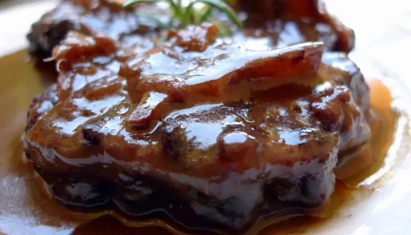 Plato de rabo de toro estofado, con una salsa oscura y brillante, adornado con una ramita de romero.