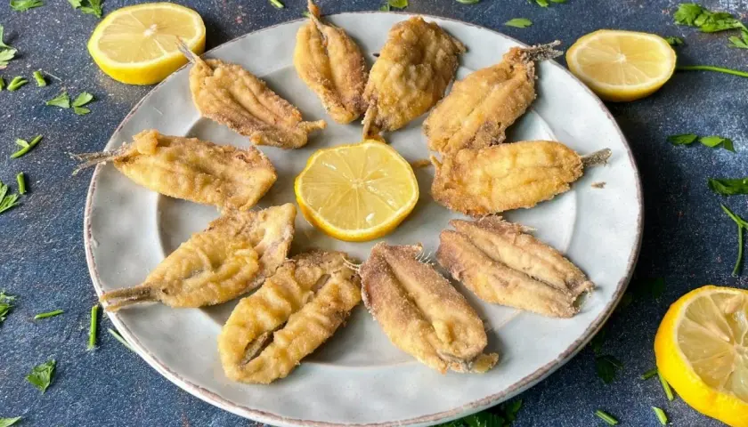 Plato de boquerones fritos crujientes, adornado con rodajas de limón y perejil fresco. Un aperitivo perfecto.