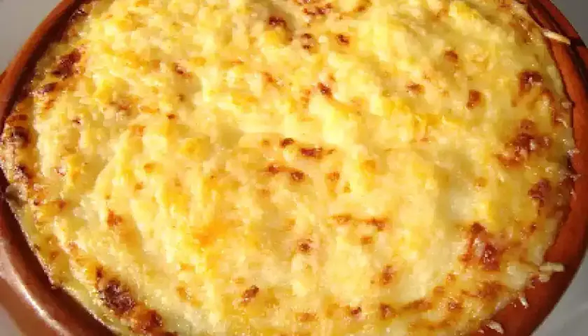 Un delicioso pure de patata gratinado, con bordes dorados y burbujeante, servido en una cazuela de barro.