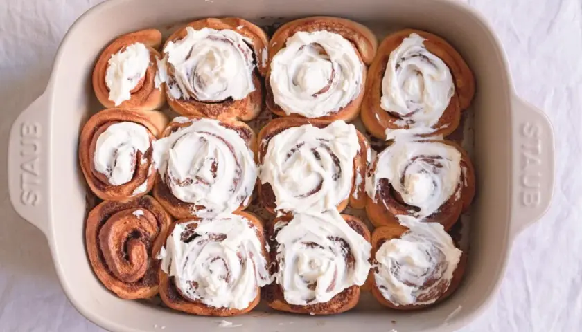 Horneados rollitos de canela cubiertos con glaseado cremoso en un molde de cerámica.